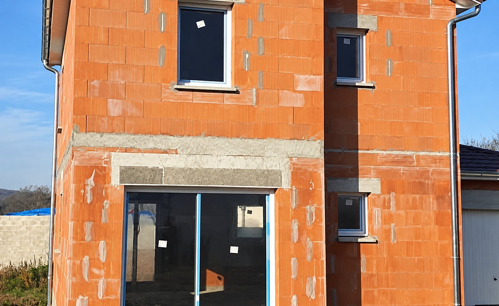 Maison à étage en briques rouges avec fenêtres et baie vitrée posées, en cours de construction